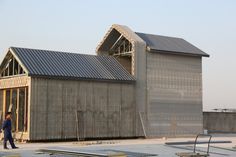 a man walking past a building with metal roofing on it's sides and another building in the background