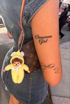 a woman with a small tattoo on her arm holding a banana keychain that says, cinnamon girl