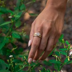 a woman's hand with a ring on top of her finger and flowers in the background