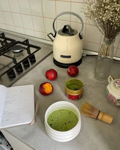 a bowl of green liquid sitting on top of a counter next to an open book