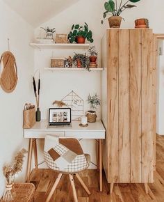 a white desk topped with a laptop computer sitting next to a wooden shelf filled with potted plants