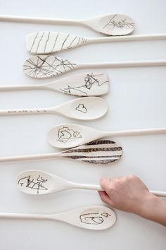 five spoons with drawings on them are being held by someone's hand over a white surface