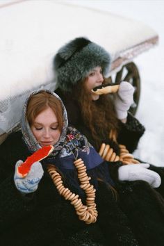 two women sitting on the ground in winter clothes and hats, one with a cell phone to her ear