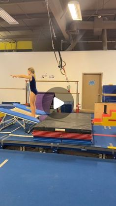 a woman standing on top of a trampoline in an indoor area with blue flooring