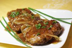 some meat and onions on a white plate with green onion garnishes in gravy