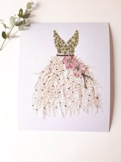 a card with a dress made out of feathers and flowers on it next to a plant