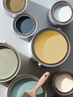 several paint cans with different colors of paint and a brush