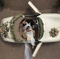 a bride and groom are in the back of a white car with flowers on it