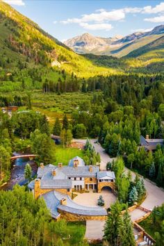 an aerial view of a large home surrounded by trees and mountains in the distance, with a river running through it