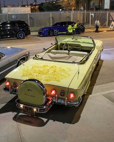 an old yellow car parked on the side of the road with other cars behind it