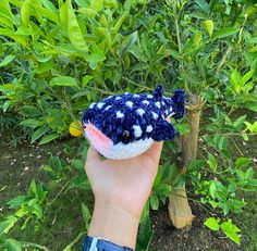 a hand holding a stuffed animal in front of some bushes