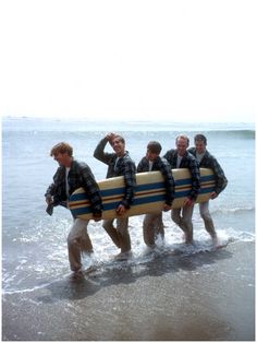 four men are carrying their surfboards into the water at the beach while wearing plaid shirts and khaki pants