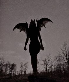 a black and white photo of a woman with wings on her back, standing in the woods