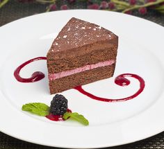 a piece of chocolate cake with raspberry sauce on a white plate next to berries