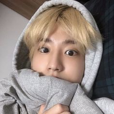 a boy with blonde hair wearing a grey hoodie and holding his hands under his face