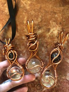 three wire wrapped pendants are being held by someone's hand on a marble surface