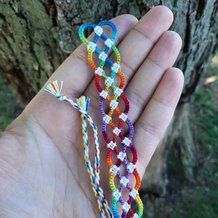 a hand holding two multicolored bracelets in front of a tree