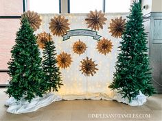 three christmas trees are on display in front of a white backdrop with gold stars and snowflakes