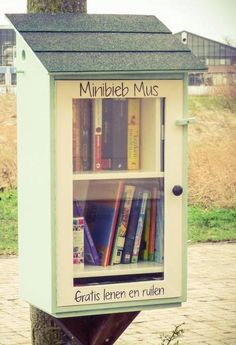 a book shelf with books on it in the middle of a sidewalk next to a tree