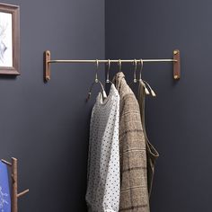 two coats hanging on a coat rack in front of a blue wall with a framed picture