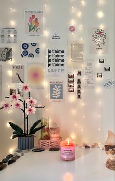 a white table topped with a vase filled with flowers next to a wall covered in pictures