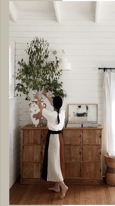 a woman standing in front of a dresser with a potted plant on top of it