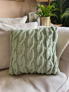 a green knitted pillow sitting on top of a couch next to a potted plant