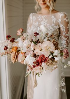 a woman holding a bouquet of flowers in her hand and wearing a white wedding dress