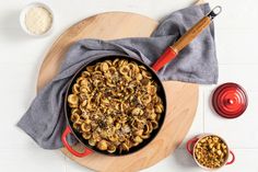 a skillet filled with pasta on top of a wooden cutting board next to two bowls