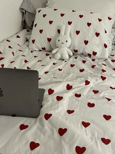 an apple laptop computer sitting on top of a bed with red hearts all over it