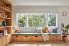 a window seat in the corner of a room with bookshelves and potted plants