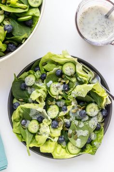 a salad with lettuce, blueberries and cucumbers in it next to a glass of milk