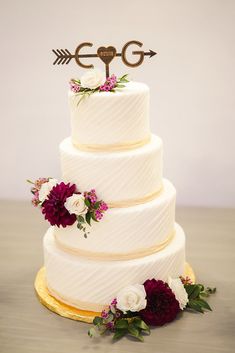 a three tiered wedding cake with flowers and an arrow topper on the side