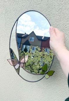 a hand holding a mirror with a reflection of a house in it and a butterfly on the side