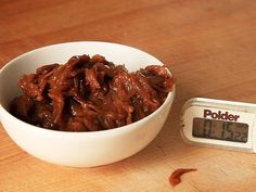 a white bowl filled with food on top of a wooden table next to a digital thermometer