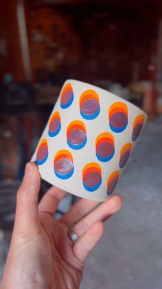 a hand holding up a small white and blue object with orange circles on the surface