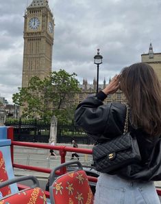 a woman standing in front of a clock tower on a cloudy day with her hand to her face