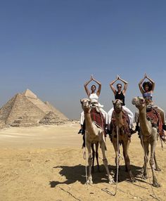 three people riding camels in front of the pyramids