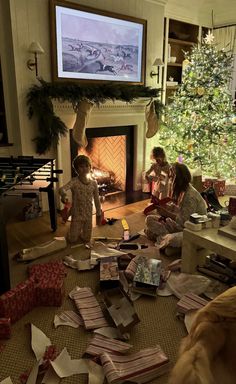 two women and a child are sitting in front of a christmas tree with presents on the floor