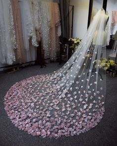 a wedding veil with pink flowers on the bottom is in front of a dress rack