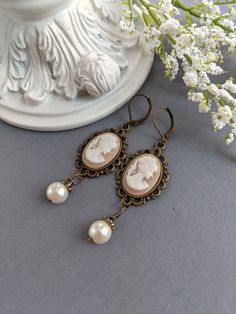 "Absolutely lovely, these soft peach cameo earrings are perfect for a Gothic or Historical period wedding! They would make an excellent gift for anyone that loves vintage-style jewelry.  Featuring ornate antique brass settings mounted with classic Grecian Goddess light peach/beige and white cameos. Adorned with an 8mm elegant, ivory glass pearl.  SIZE: Suspended by lever back ear wires the total length is about 62 mm (2 1/2\") long including the ear wires. If you prefer hook-style ear wires, ple Classic Dangle Jewelry For Vintage Events, Classic Drop Earrings For Vintage Events, Elegant Cameo Jewelry For Wedding, Cameo Drop Earrings Jewelry Gift, Cameo Drop Earrings As Gift, Gift Cameo Drop Earrings Jewelry, Elegant Cameo Earrings, Elegant Cameo Jewelry, Elegant Cameo Jewelry For Formal Occasions