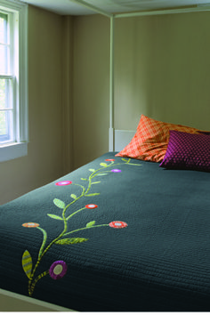 a bed with a green bedspread and colorful pillows on it next to a window