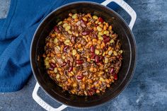 a pot filled with beans and meat sitting on top of a blue cloth next to a pair of jeans