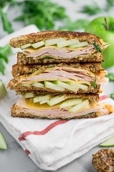 two sandwiches stacked on top of each other with apples and cucumbers in the background