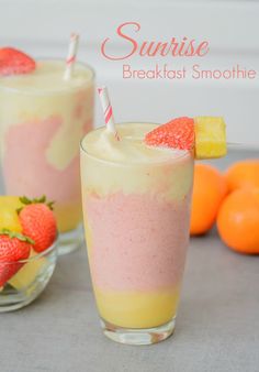 two glasses filled with smoothie next to oranges and strawberries