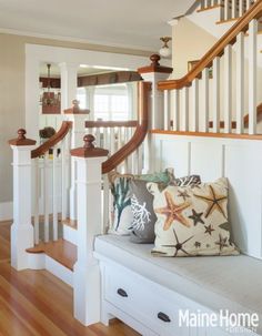 a white bench sitting under a stair case next to a wooden bannister with starfish pillows on it