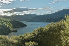 a lake surrounded by trees and mountains under a blue sky with clouds in the distance