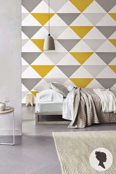 a modern bedroom with yellow and grey triangles on the wall, white bedding and rugs