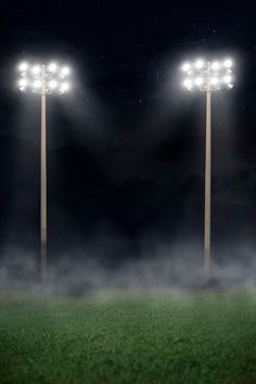 three light poles in the grass at night with fog coming from them and some lights on