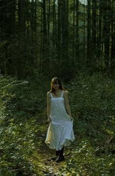 a woman in white dress walking through the woods